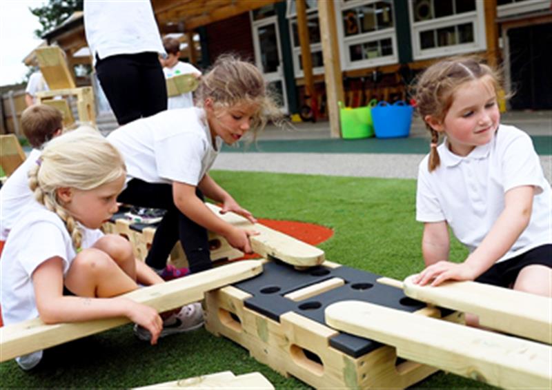 Three children working together to place Play Builder planks and blocks in certain places to make a design.